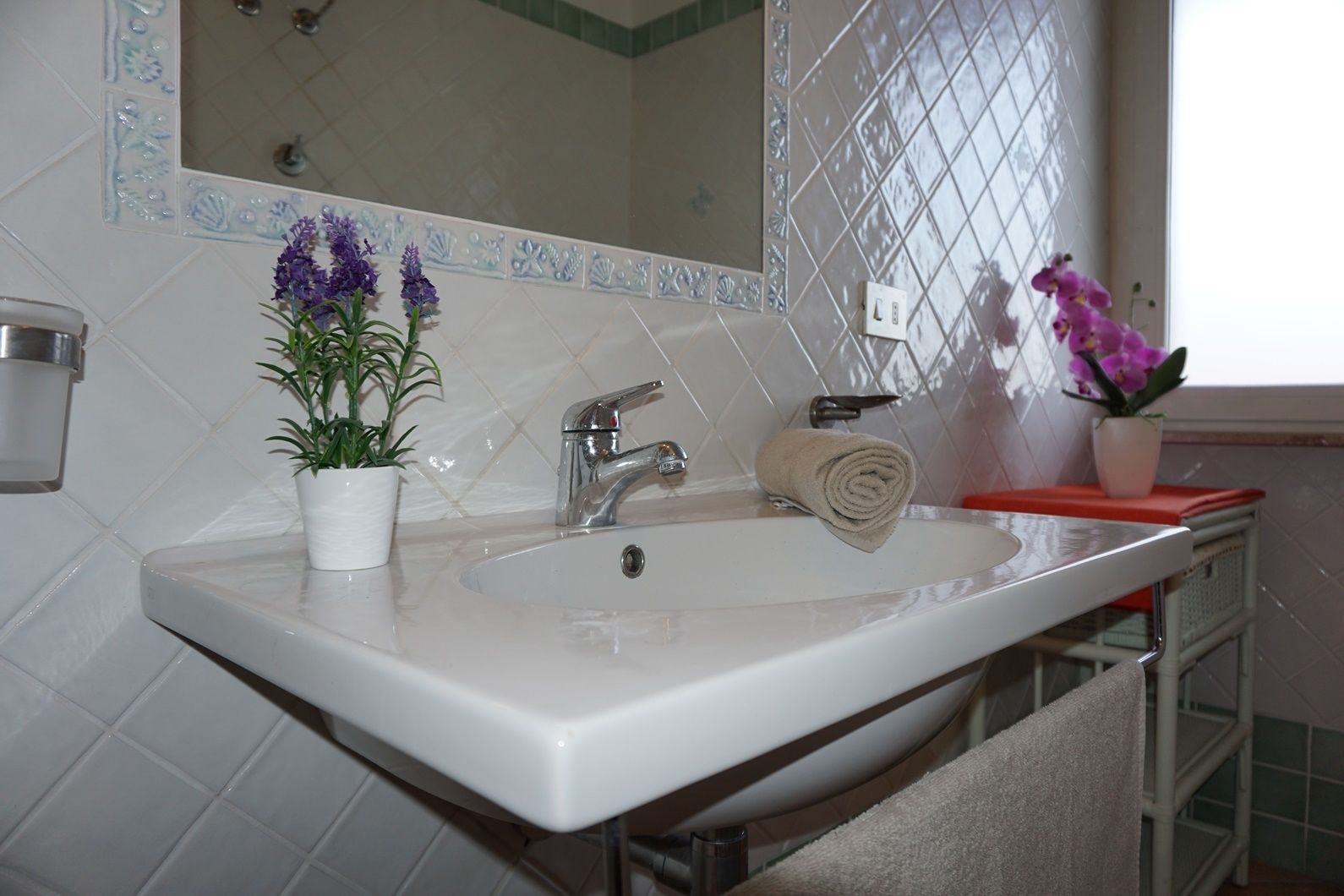 Un baño con un lavamanos blanco, un espejo y dos macetas con flores moradas.