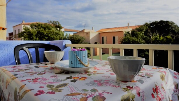 A table with a floral tablecloth, a blue container with anchors, a white bowl, and a gray bowl on a balcony with a view of buildings and trees. - Residence Levante (Santa Teresa di Gallura)