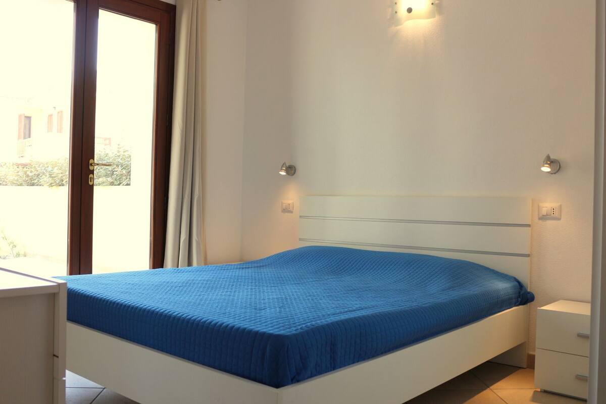 A bedroom with a bed, a nightstand, and a window with curtains.