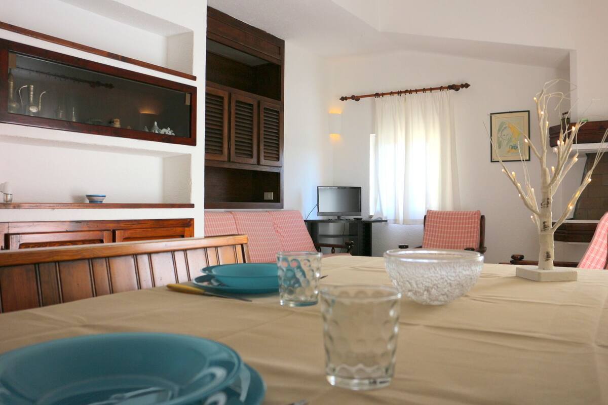 A dining area with a table set for two, a television in the background, and a decorative tree.
