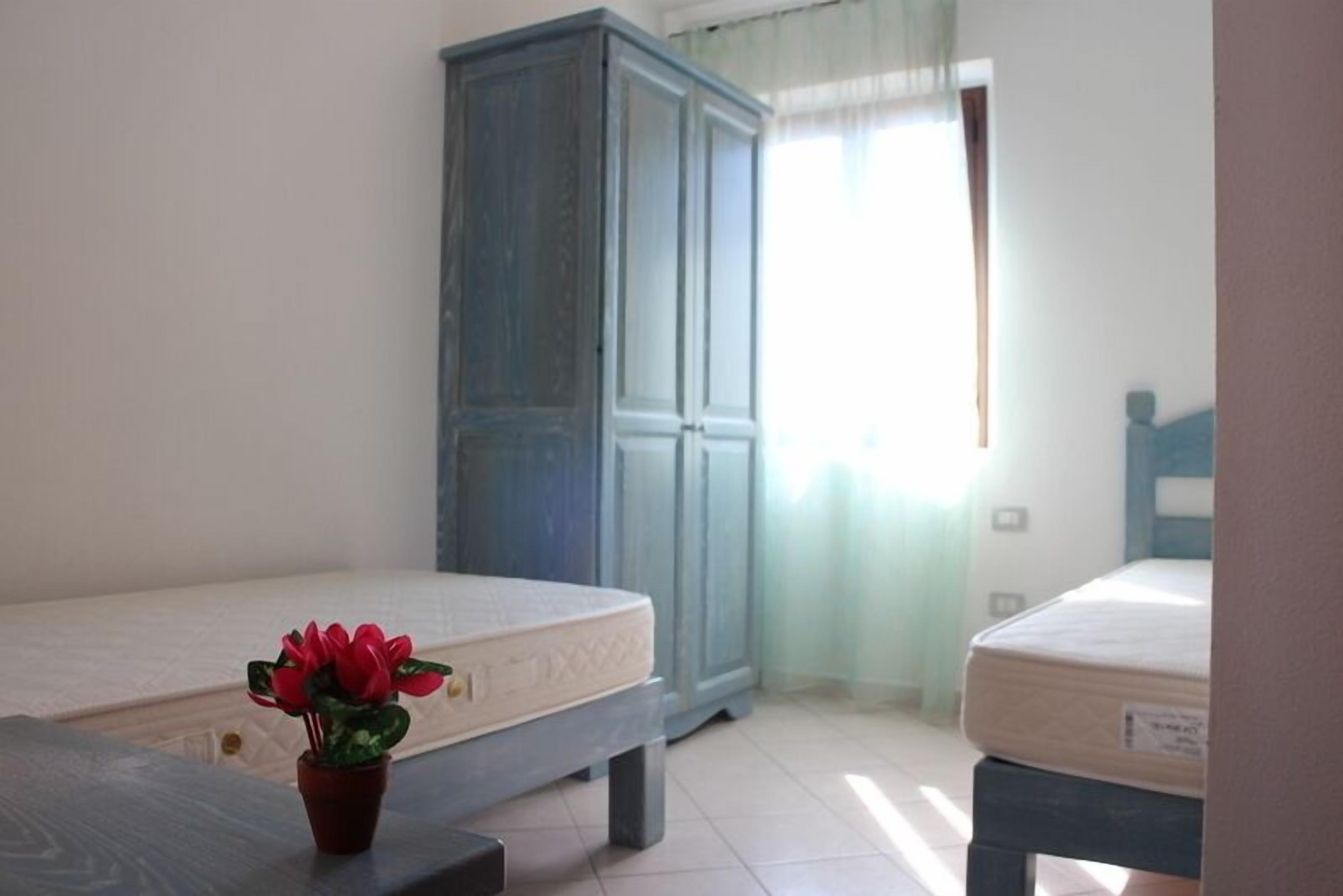 Une chambre avec deux lits, une armoire et une plante en pot.