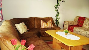 A living room with a brown leather sofa, a wooden coffee table, and a patterned armchair. There are three red roses on the sofa and a potted plant with red flowers on the coffee table. - Ferienwohnung Familie Kappauf & Petrik (Friedenfels)