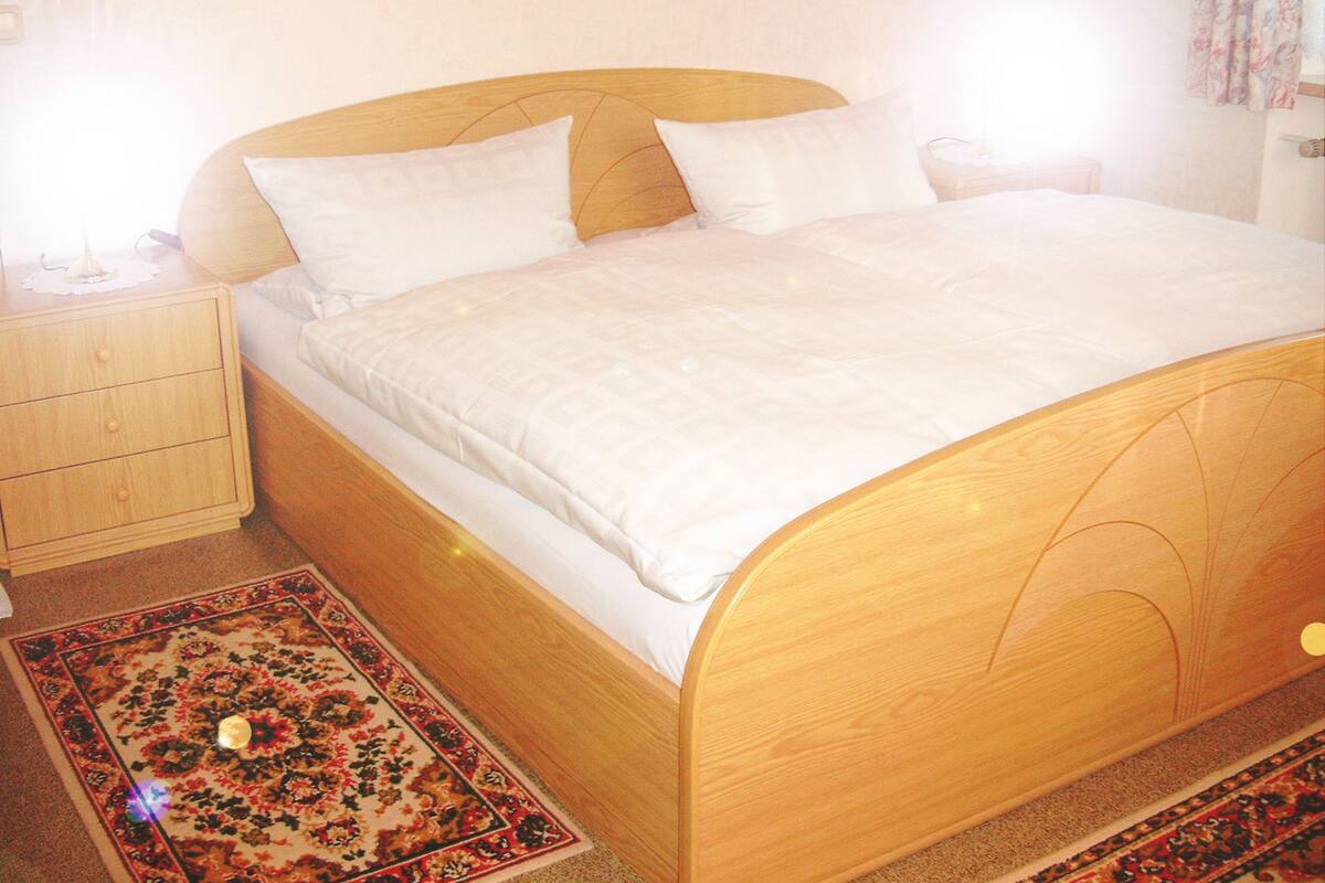 Ein Einzelbett mit Holzgestell und weißer Bettwäsche in einem Zimmer mit einem kleinen Holznachttisch und einem dekorativen Teppich.