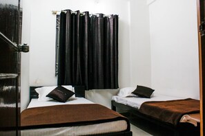 A room with two beds, each with a brown blanket and pillows, a black curtain, and a white wall. - Transit Dorms - Hostel (Bengaluru)
