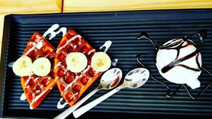 A dessert plate with waffles topped with bananas and syrup, accompanied by a scoop of ice cream and two spoons. - Transit Dorms - Hostel (Bengaluru)