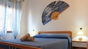 A neatly made bed with a blue bedspread, a wooden headboard, and two bedside lamps. - Rena Bianca Apartment (Santa Teresa di Gallura)