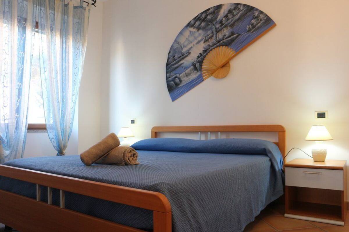 A neatly made bed with a blue bedspread, a wooden headboard, and two bedside lamps.