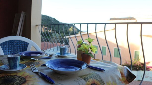 A table set for two with plates, cups, and cutlery, overlooking a scenic view. - Rena Bianca Apartment (Santa Teresa di Gallura)