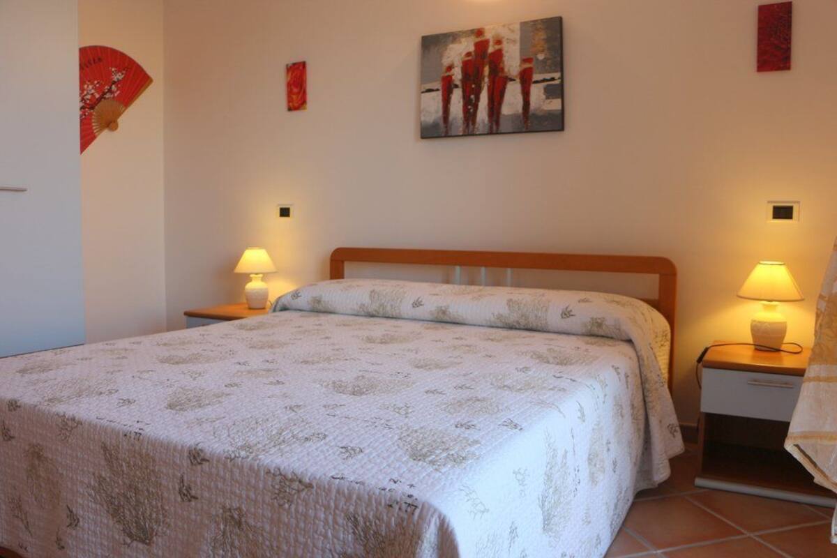 A neatly made bed with a floral bedspread, two bedside tables with lamps, and a painting on the wall.