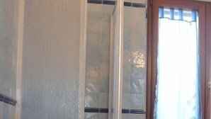 A bathroom with a shower, a potted plant, and a shelf unit. - Rena Bianca Apartment (Santa Teresa di Gallura)