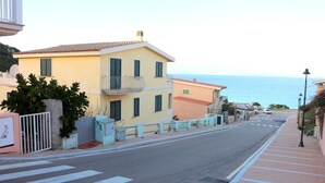 A coastal street with a yellow building, a pedestrian crossing, and a view of the sea. - Rena Bianca Apartment (Santa Teresa di Gallura)