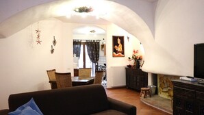A living room with a sofa, dining area with chairs, a TV, and a decorative wall. - Casette del Centro (Santa Teresa di Gallura)
