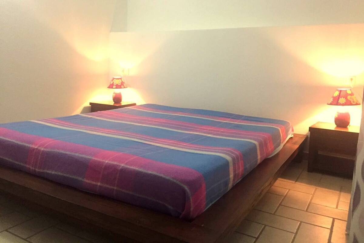 A single bed with a striped bedspread, two bedside tables with lamps, and a tiled floor.