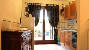 A compact kitchen with wooden cabinets, a refrigerator, and a window with curtains. - Casette del Centro (Santa Teresa di Gallura)