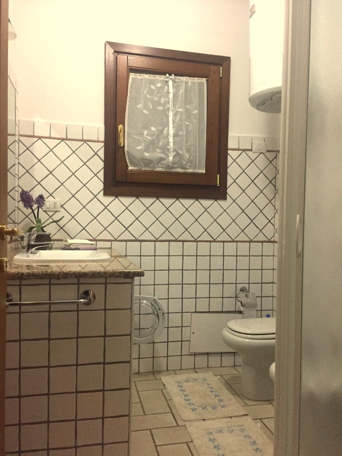 A small bathroom with a toilet, sink, and a window with a curtain.