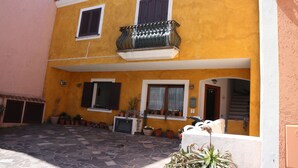 A two-story building with a yellow facade, a balcony with a metal railing, and multiple windows with shutters. - Casette del Centro (Santa Teresa di Gallura)