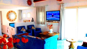 A living room with a blue sofa, a coffee table, a TV, and a decorative vase. - Rena Bianca Beach House (Santa Teresa di Gallura)