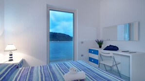 A bedroom with a bed, a desk, a chair, a lamp, a potted plant, and a view of the sea. - Rena Bianca Beach House (Santa Teresa di Gallura)