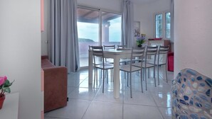 A dining area with a white table and chairs, a red sofa, and a view through large glass doors to an outdoor terrace. - Rena Bianca Beach House (Santa Teresa di Gallura)