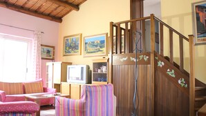 A cozy living room with a wooden staircase, a television, and a striped armchair. - Casa Seby (Santa Teresa di Gallura)
