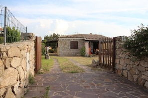 A stone house with a tiled roof, a stone pathway leading to the entrance, and a wooden fence. - Villetta Sartori (Santa Teresa di Gallura)