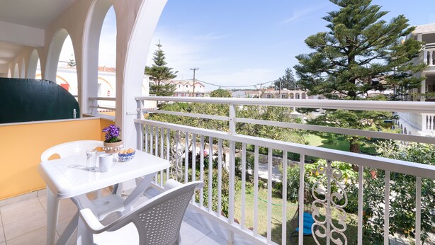 A balcony with a white railing, a table with chairs, and a potted plant. - Domus Alta (Zakynthos)