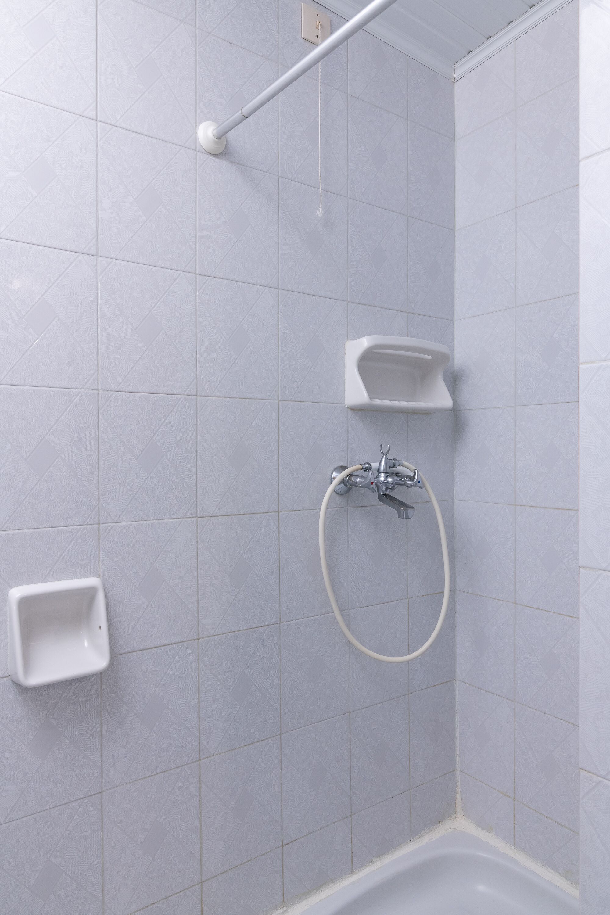 A corner of a bathroom with a shower, a handheld showerhead, and a small sink.