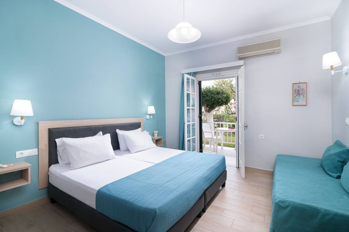Un dormitorio con cama, mesita de noche, ventana y puerta que da a un espacio exterior.