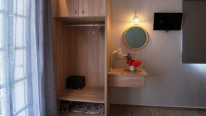 A room with a wooden wardrobe, a mirror with a round frame, a small shelf with a vase of flowers, and a television mounted on the wall. - Domus Alta (Zakynthos)