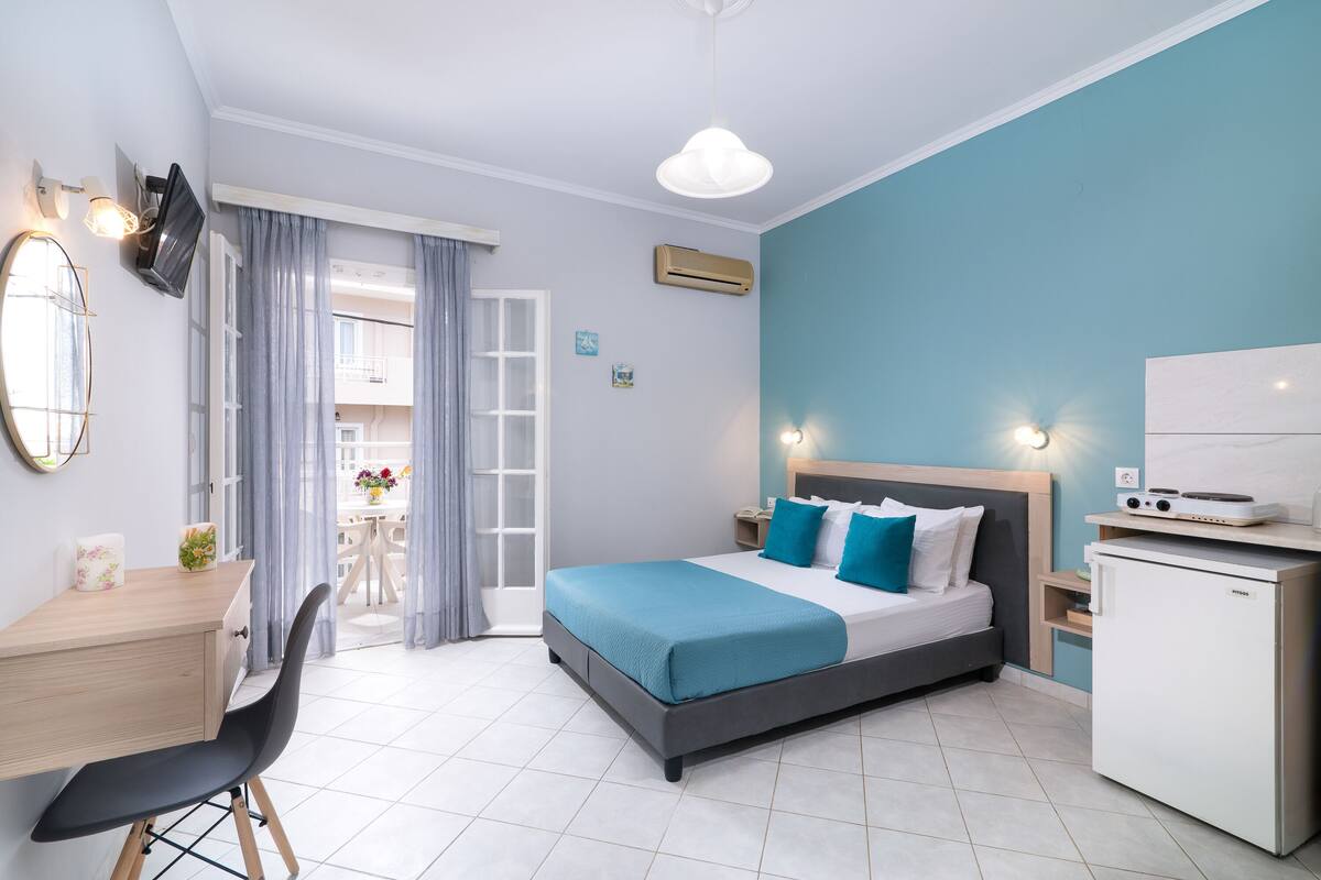 Un dormitorio moderno con cama, escritorio, silla y una pequeña kitchenette.