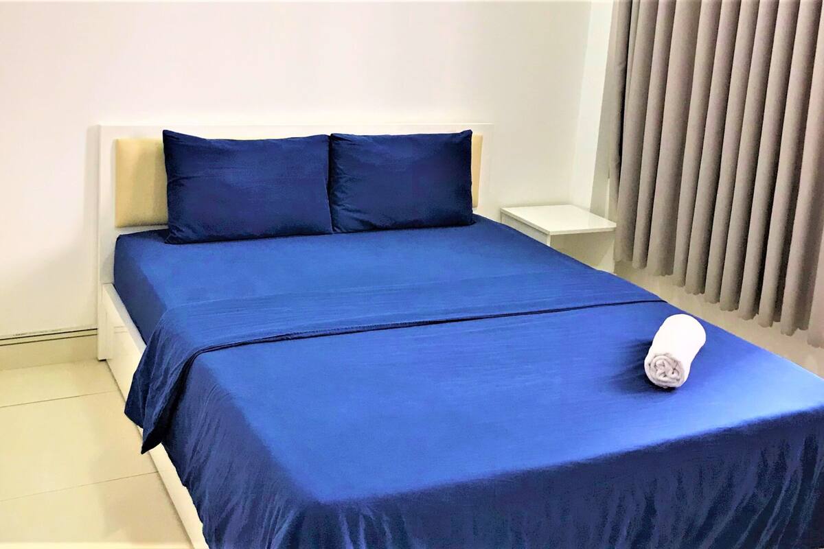 Ein Hotelzimmer mit einem aufgeräumten Bett, einem weißen Nachttisch und einem Fenster mit Vorhängen.