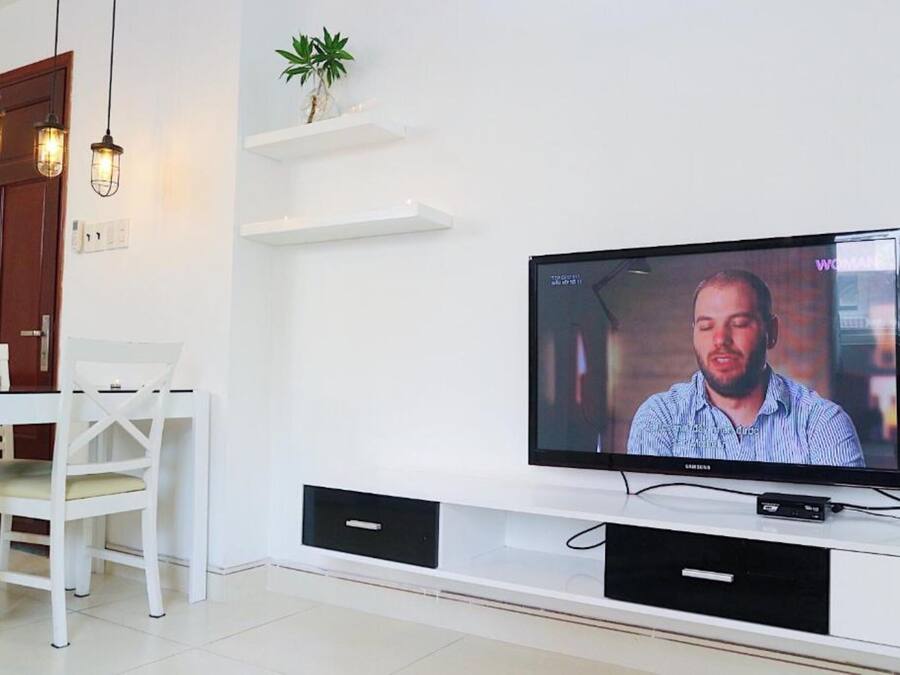 Una sala de estar moderna con un televisor de pantalla plana montado en un mueble blanco, una puerta de madera y una mesa de comedor blanca con sillas.