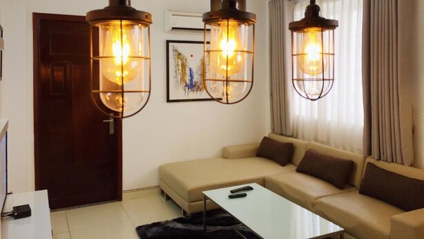 Uma sala de estar com um sofá bege, uma mesa de centro branca e duas luminárias pendentes.