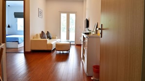 Uma sala de estar moderna com um sofá, um banquinho e uma televisão sobre um móvel.
