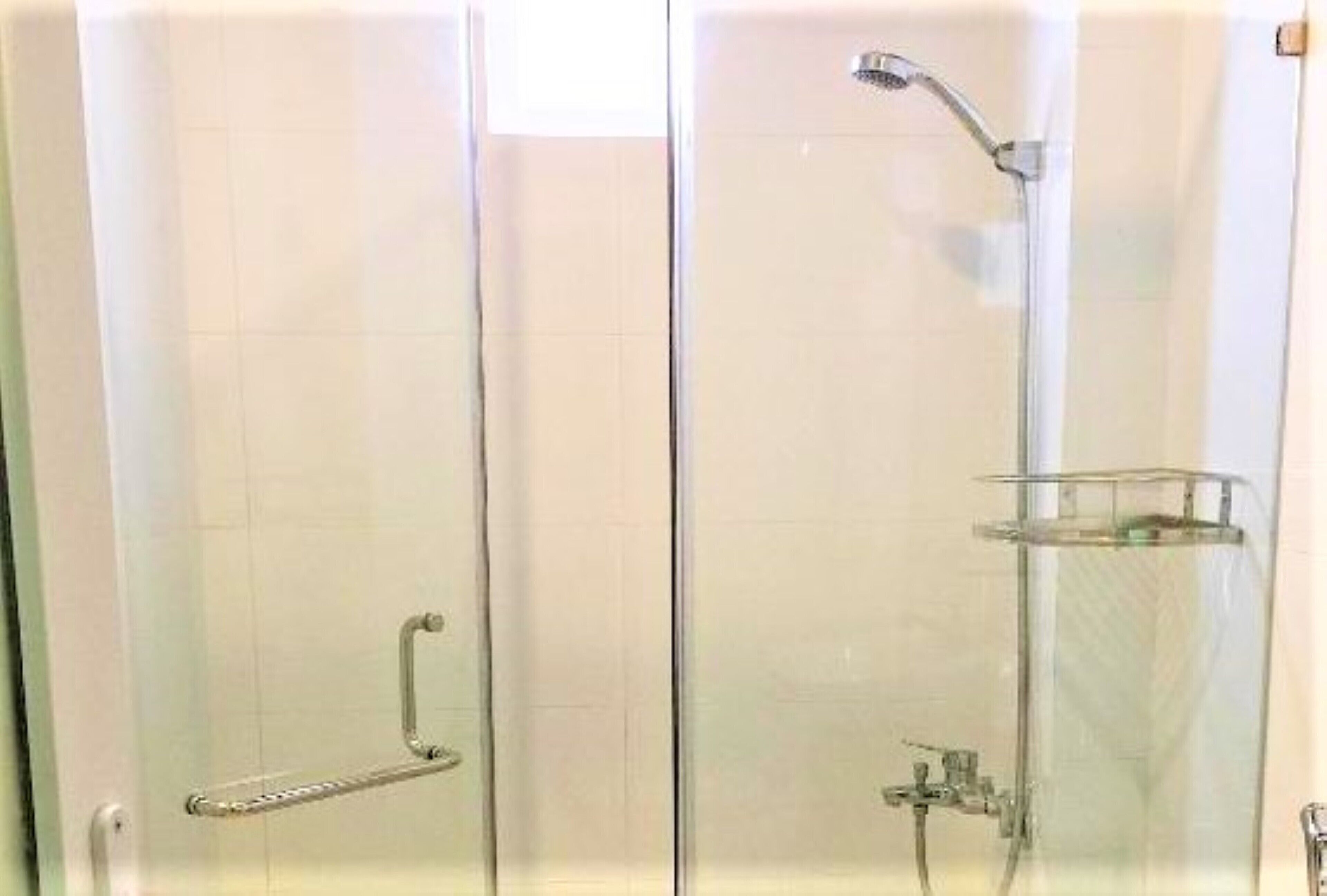 A glass-enclosed shower with a handheld showerhead and a wall-mounted faucet.