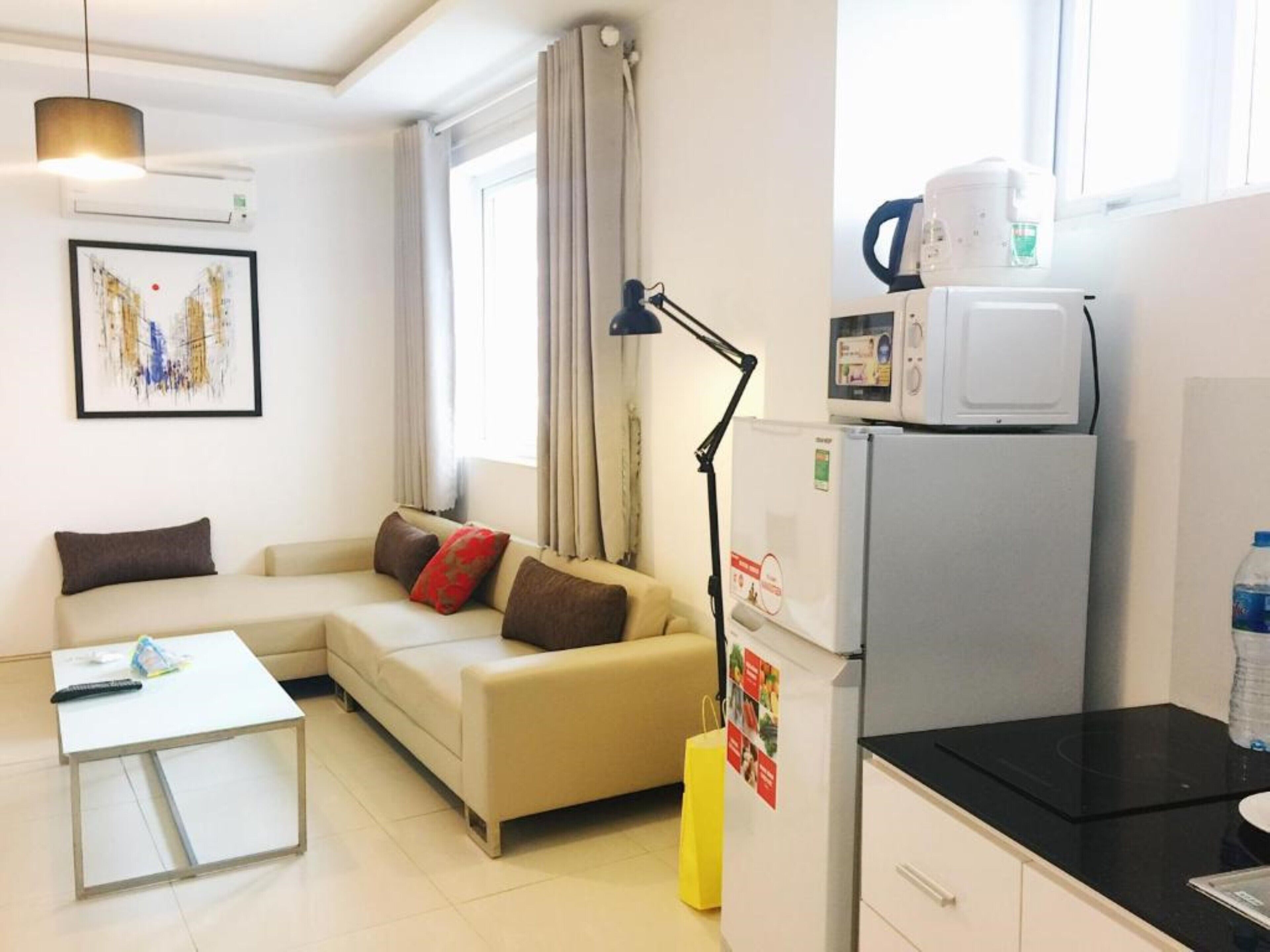 Ein modernes Wohnzimmer mit einer Couch, einem Couchtisch, einer Lampe, einem Kühlschrank und einer Mikrowelle.