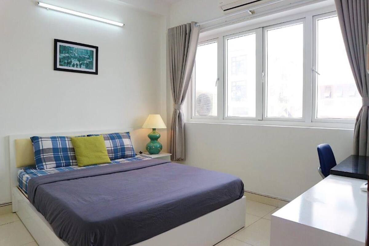 Ein Schlafzimmer mit Bett, Schreibtisch, Lampe und einem Fenster mit Vorhängen.