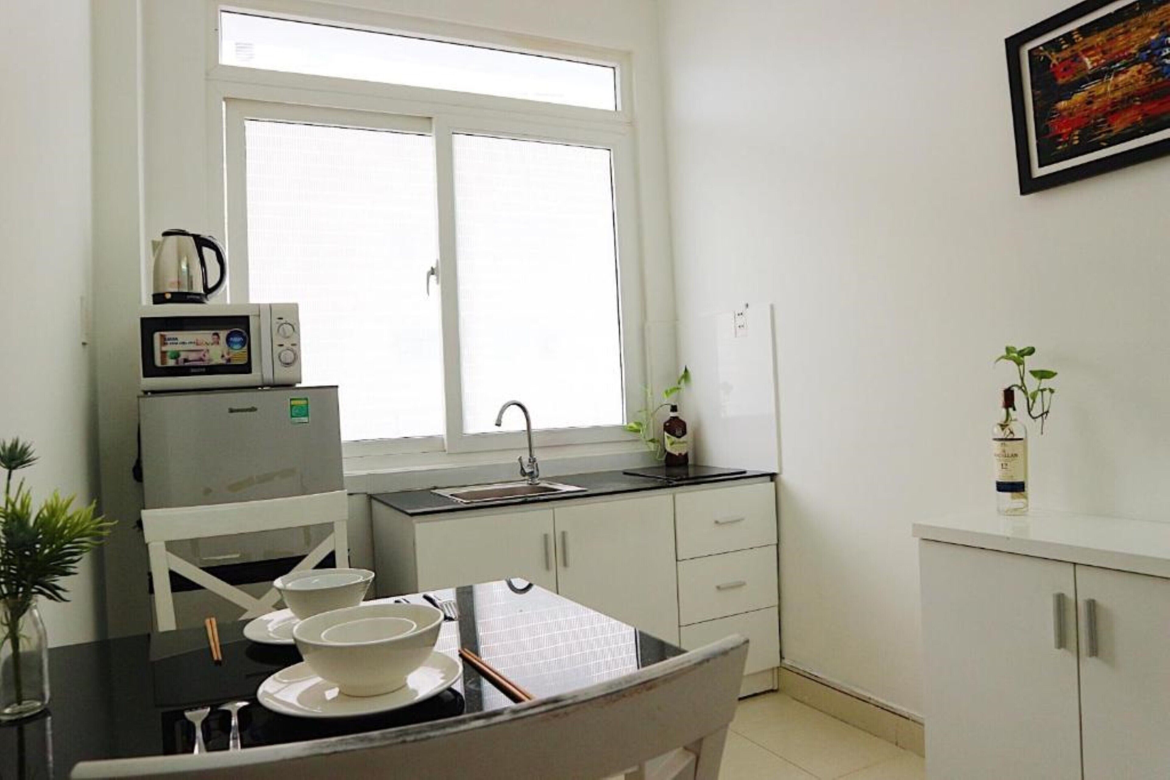 A compact kitchen with white cabinets, a black countertop, a microwave, a sink, and a window.