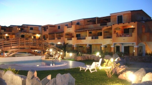 Ein Hotelinnenhof mit einem zentralen Pool, Liegestühlen und einer Holzbrücke.