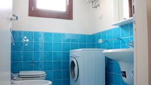 Ein kleines Badezimmer mit blauen Fliesen, einer Waschmaschine, einer Toilette und einem Waschbecken.