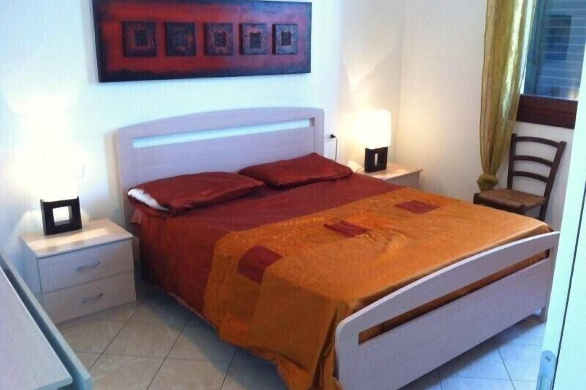 A bedroom with a bed, nightstands, a chair, and a wall-mounted artwork.