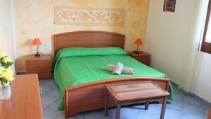 Ein Schlafzimmer mit einem hölzernen Bett, einer grünen Tagesdecke, zwei Nachttischen mit Lampen, einem Holzbeistelltisch und einer kleinen Holzbank.