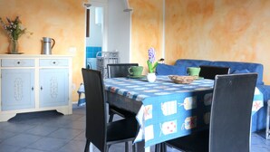 Ein Essbereich mit einem Tisch für vier Personen, Stühlen, einem Schrank mit dekorativen Griffen und einer blau-weißen Tischdecke.