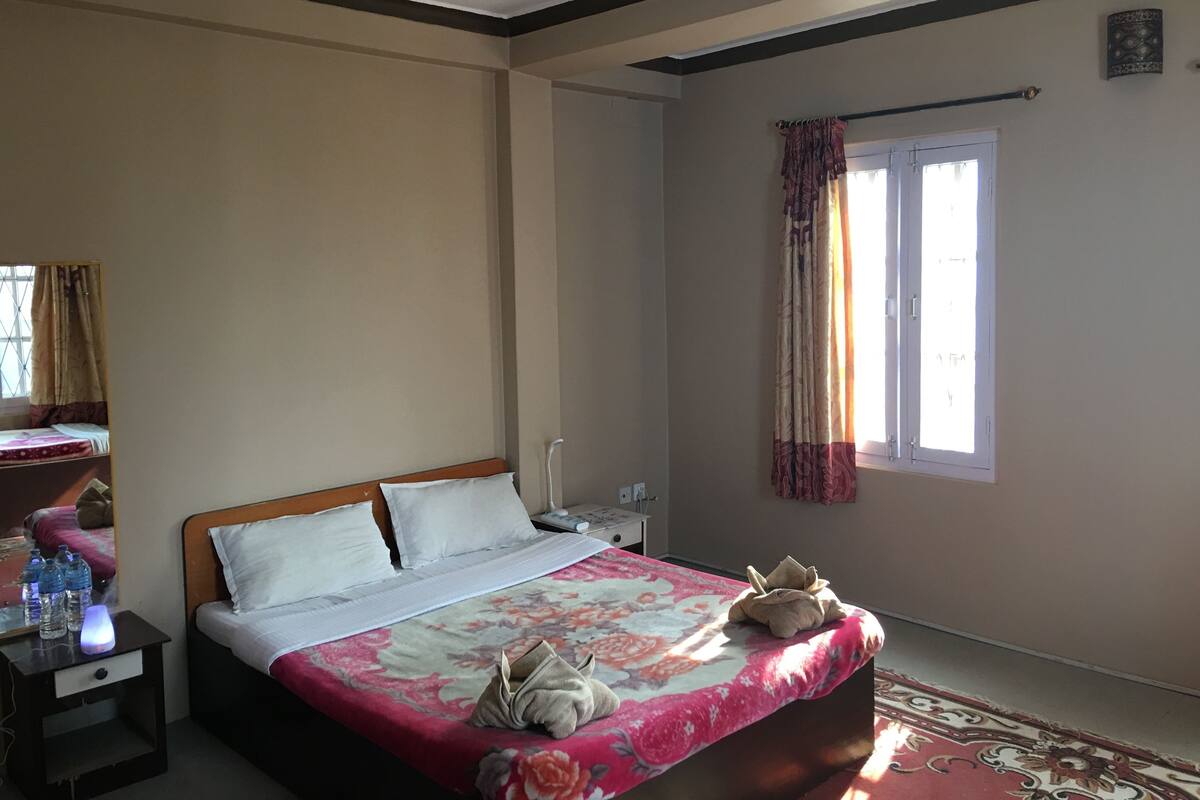 A bedroom with a bed, bedside table, and a window with curtains.