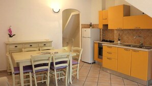 A compact kitchen with a dining table and chairs, a refrigerator, and yellow cabinets. - Gemelle di Cairoli (Santa Teresa di Gallura)