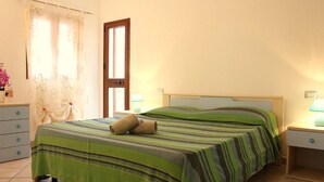 A neatly made bed with green and brown striped bedding, a wooden door, a nightstand with a lamp, and a dresser with drawers. - Gemelle di Cairoli (Santa Teresa di Gallura)