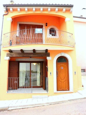A two-story building with a balcony, a wooden door, and a window with curtains. - Gemelle di Cairoli (Santa Teresa di Gallura)