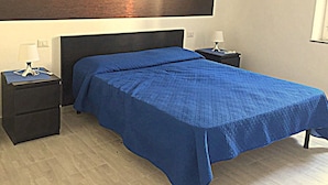 A bedroom with a large bed, two bedside tables, and a wall-mounted artwork depicting a sunset over water. - Tiffany House (Santa Teresa di Gallura)