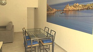 A dining area with a glass table and chairs, a grey sofa, and a painting of a coastal landscape on the wall. - Tiffany House (Santa Teresa di Gallura)