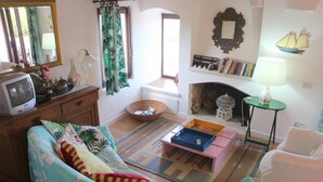 Un salon chaleureux avec un canapé, une petite table, une bibliothèque, une cheminée et un téléviseur posé sur un meuble en bois.